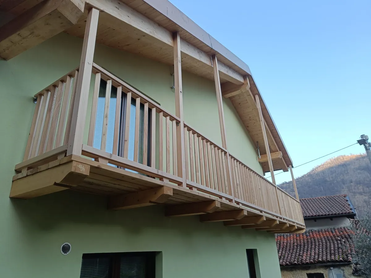 Tinteggiatura di una facciata: una casa col balcone in legno, tinteggiata di verde chiaro